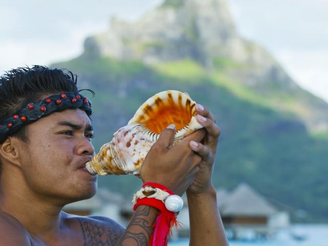 Young man blowing in a pahu (shell) in front of the Mount Otemanu